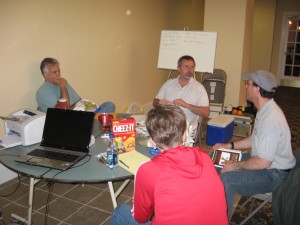 The writing team hard at work: On the left, facing camera, screenwriter Pat Potochick; to his right, screenwriter and producer Bernie Tague; with the ball cap and STC! in his hand is screenwriter and Save the Cat! alumnus Barry Cutler; with her back to the camera, screenwriter Carrie Doyle.